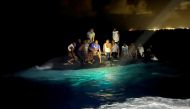 Survivors of a migrant boat that capsized perch on the overturned vessel off the coast of New Providence Island, Bahamas, July 24, 2022. (Royal Bahamas Defence Force/Handout via REUTERS)

