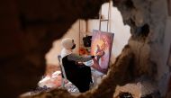 A Palestinian artist draws a painting inside the damaged house of Gaza artist, Duniana Al-Amour, who had been killed during Israel-Gaza fighting, in Khan Younis in the southern Gaza Strip, August 23, 2022. (REUTERS/Ibraheem Abu Mustafa)