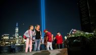 People pay respect for the victims at a memorial while the Tribute in Light art installation and the One World Trade Center are seen in the background on the 20th anniversary of the September 11, 2001 attacks in New York City, as it is seen from Exchange Place, New Jersey, US, on September 11, 2021. REUTERS/Eduardo Munoz