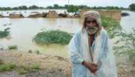 A flood victim covers himself with a plastic sheet to avoid rain, with damaged houses in the background, following rains and floods during the monsoon season in Jafarabd, Pakistan August 26, 2022. REUTERS/Amer Hussain