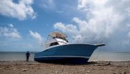 A man stands next to a washed up boat on the beach after Hurricane Fiona in Santa Isabel, Puerto Rico September 21, 2022. REUTERS/Ricardo Arduengo
