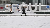 A woman walks along a snow-covered street in front of City Hall during snowfall in Seoul on January 26, 2023. (Photo by Jung Yeon-je / AFP)