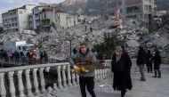 A man holds debris in front of destroyed buildings in the Antakia historical city in Hatay on February 11, 2023, after a 7.8-magnitude earthquake struck the country's south-east. Photo by BULENT KILIC / AFP