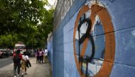 In this file photo taken on October 18, 2022, students walk past a wall painted with an anti-bitcoin protest symbol, in San Salvador. (Photo by Marvin Recinos / AFP)
