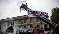 A Greenpeace activist holds a flare as he stands at the top of a fire truck ladder after activists unfolded a banner reading 'Amazon on fire Macron still complicit' in front of The Elysee Palace in Paris on September 10, 2020. (Photo by Christophe Archambault / AFP)