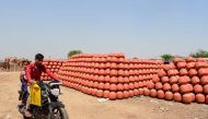 A motorist drives past a stack of clay pots which are popularly used to store drinking water during the summer season, at a village on the outskirts of Ahmedabad on March 27, 2023. (Photo by SAM PANTHAKY / AFP)


