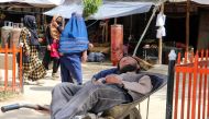 An Afghan daily worker sleeps on his wheelbarrow while women walk past at a market in Fayzabad district of Badakhshan province on April 10, 2023. (Photo by OMER ABRAR / AFP)