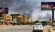 Smoke rises in the background as a car drives along an almost deserted street in Khartoum on April 16, 2023, during ongoing fighting between the forces of 2 rival generals. (Photo by AFP)