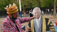 A Royal fan adjusts a life-sized cut-out of Britain's King Charles III, on The Mall in central London, on May 4, 2023, ahead of the coronation weekend. (Photo by SEBASTIEN BOZON / AFP)