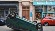 A police officer stands by a car which is upside down on a street following a fourth consecutive night of rioting in France sparked by the death of teenage driver Nahel by a police bullet, in Lyon, south-eastern France on July 1, 2023. Photo by OLIVIER CHASSIGNOLE / AFP)
