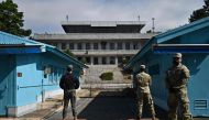 UNC (United Nations Command) soldiers (R) and a South Korean soldier (L) stand guard before North Korea's Panmon Hall (rear C) and the military demarcation line separating North and South Korea, at Panmunjom, in the Joint Security Area (JSA) of the Demilitarized Zone (DMZ) on October 4, 2022.
