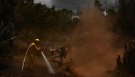 A Maui County firefighter uses a hose line to extinguish a fire near homes during the upcountry Maui wildfires in Kula, Hawaii on August 13, 2023. Photos by Patrick T. Fallon / AFP