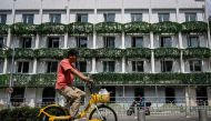 A man rides a bicycle past a building under renovation at a shopping mall in Beijing on August 15, 2023. (Photo by Jade Gao / AFP)