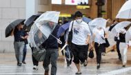 Pedestrians try to shield from wind and rain as they cross the street in front of Osaka Station on August 15, 2023, as Tropical Storm Lan hit the main island of Honshu overnight. Photo by JIJI Press / AFP