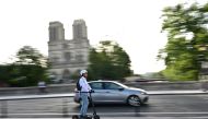A man rides his electric scooter or trottinette past the Notre-Dame de Paris Cathedral in Paris on August 23, 2023. (Photo by MIGUEL MEDINA / AFP)

