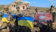 This handout photograph released by Ukrainian presidential chief of staff Andriy Yermak on September 17, 2023, shows Ukrainian servicemen posing for a photo with Ukrainian national flags in front of a destroyed building in the village of Klyshchiivka, Donetsk region. (Photo by Handout / Ukrainian Presidential Chief of Staff Andriy Yermak / AFP)