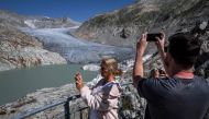 (Files) A photograph taken on August 24, 2023 above Gletsch, in the Swiss Alps shows tourists taking a picture of the Rhone Glacier and its glacial lake due to the melting of the glacier. (Photo by Fabrice Coffrini / AFP)
 