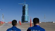 Staff members stand before a Long March-2F carrier rocket, carrying the Shenzhou-17 spacecraft, on the launch pad encased in a shield at the Jiuquan Satellite Launch Centre in the Gobi desert in northwest China on October 25, 2023. Photo by Pedro PARDO / AFP