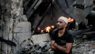 An injured man sits in front of a smouldering building in the aftermath of an Israeli strike on Gaza City on October 26, 2023, as battles continue between Israel and the Palestinian Hamas group. Photo by Omar El-Qattaa / AFP