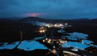 The red shimmer from magma is seen coming out from the erupting Fagradalsfjall volcano behind the tourist land mark Blue Lagoon, near the town of Grindavik some 40 km west of the Icelandic capital Reykjavik, on March 20, 2021. Photo by Halldor KOLBEINS / AFP