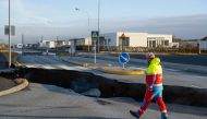 This photo taken on November 13, 2023 shows a member of the emergency services walking near a crack cutting across the main road in Grindavik, southwestern Iceland following earthquakes. Photos by Kjartan TORBJOERNSSON / AFP