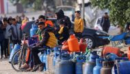 People sit with empty canisters waiting for them to be filled with cooking gas from a tank that entered the Palestinian enclave via the Rafah crossing with Egypt on November 25, 2023. (Photo by SAID KHATIB / AFP)