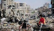 A Palestinian youth sits next to his bicycle amid the rubble of destroyed buildings in Gaza City on the northern Gaza Strip following weeks of Israeli bombardment, as a four-day ceasefire took effect on November 24, 2023. Photo by AFP