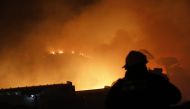 A South African firefighter is seen near a house surounded by flames as a fire rages on the mountain above Simon's Town on December 20, 2023. (Photo by GIANLUIGI GUERCIA / AFP)