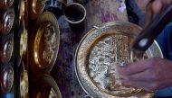A Tunisian artisan engraves a design onto a copper plate at his shop in the souks of the medina of Tunis on December 7, 2023. (Photo by Fethi Belaid / AFP)