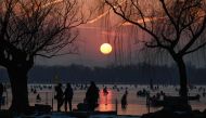 People ride sleds on a frozen lake at the Summer Palace during sunset in Beijing on December 28, 2023. (Photo by JADE GAO / AFP)