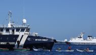 This photo taken on February 15, 2024 shows Filipino fishermen aboard their wooden boats queueing for free fuel beside the Philippine Bureau of Fisheries and Aquatic Resources (BFAR) ship BRP Datu Tamblot (L) as a Chinese coast guard ship (background R) monitors near the China-controlled Scarborough Shoal, in disputed waters of the South China Sea. (Photo by Ted Aljibe / AFP)