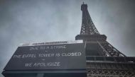This photograph taken on February 19, 2024, in Paris, shows a board informing visitors that the Eiffel Tower, viewed in the background, is closed as staff go on strike, over the financial management of the monument by the city, closing the monument to the public during the second week of the French school holidays. Photo by Kiran Ridley / AFP