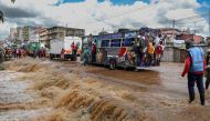 Pedestrians hang off the back of a matatu (public transport bus) to avoid having to wade across a flooded section of road after a stream burst it's banks overnight following heavy seasonal rain in the capital, Nairobi on April 24, 2024. (Photo by Tony KARUMBA / AFP)
