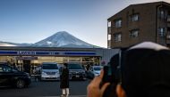 This photo taken on January 1, 2024 shows a tourist posing in front of a convenience store with Mount Fuji in the background, in the town of Fujikawaguchiko, Yamanashi prefecture. Photo by Philip FONG / AFP