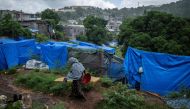 (FILES) A woman walks on a muddy pathway along shelter tents in a makeshift camp where migrants live at the Cavani stadium in Mamoudzou on the French island of Mayotte, on February 15, 2024. (Photo by JULIEN DE ROSA / AFP)

