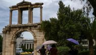 (Files) Tourists holding umbrellas walk in front of the ancient Roman Andrian Gate, during a hot day in Athens on June 13, 2024. (Photo by Aris Messinis / AFP)