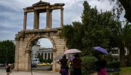 (FILES) Tourists holding umbrellas walk in front of the ancient Roman Andrian Gate, during a hot day in Athens on June 13, 2024. (Photo by Aris MESSINIS / AFP)
