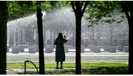 A woman stands on August 27, 2024 in front of a sprinkler watering the lawn close to the Chancellery in Berlin, where temperatures were expected to reach up to 30 degrees Celsius during the following days. (Photo by Tobias SCHWARZ / AFP)
