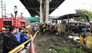 Firefighters and rescue workers stand next to a burnt-out bus that was carrying students and teachers on the outskirts of Bangkok, on October 1, 2024. (Photo by Manan VATSYAYANA / AFP)
