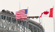 (FILES) The US and Canadian flags fly on the US side of the St. Clair River near the Bluewater Bridge border crossing between Sarnia, Ontario and Port Huron, Michigan on January 29, 2025. (Photo by Geoff Robins / AFP)
