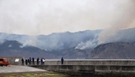 This picture taken on March 3, 2025 shows people watching a wildfire which approaches a village from the fishing port of Ofunato city in Iwate prefecture. (Photo by JIJI PRESS / AFP) 