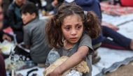 A Palestinian child carrying food cries as people gather for a mass fast-breaking iftar meal in Beit Lahia in the northern Gaza Strip on March 15, 2025. (Photo by Omar Al-Qattaa / AFP)
