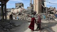 Palestinians walk past debris of buildings destroyed during the aggression in Gaza City on March 28, 2025. Photo by Omar AL-QATTAA / AFP.
