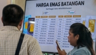 A customer uses her smartphone while conducting a gold transaction as a monitor displays the gold price per gram at Galeri 24 owned by Pegadaian, state owned pawnshop, in Jakarta on April 14, 2025. (Photo by BAY ISMOYO / AFP)
