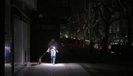 A woman uses her phone's torch while she walks her dog as the street lies in complete darkness during a massive power cut affecting the entire Iberian peninsula and the south of France, in Vigo on April 28, 2025. Photo by MIGUEL RIOPA / AFP