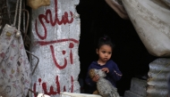 A girl stands near graffiti on a concrete pillar with names of Palestinian father Wissam Wishah's children, Said, Salma, and Eline who were killed in Israeli strikes in the vicinity of their home, at their heavily damaged house at the Al Bureij refugee camp in the central Gaza Strip on May 1, 2025. (Photo by Eyad Baba / AFP)
