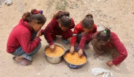 Palestinian girls eat hot food from rations provided at a charity kitchen set up at the Islamic University campus in Gaza City on May 12, 2025. (Photo by Omar AL-QATTAA / AFP)

