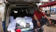 A Palestinian man sits by shrouded bodies killed in Israeli strikes, in the back of a van outside Al-Shifa hospital in Gaza City on May 18, 2025. (Photo by Bashar TALEB / AFP)
