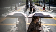 A woman uses an umbrella to shield from the sun as she walks down a street at the Yurakucho district in Tokyo where temperatures have topped 34 degrees Celsius on June 18, 2025. (Photo by Philip Fong / AFP)