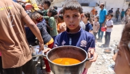 A Palestinian boy carries a pot with food collected at a charity kitchen providing hot meals in Rimal neighbourhood in Gaza City on June 18, 2025. Photo by Omar AL-QATTAA / AFP